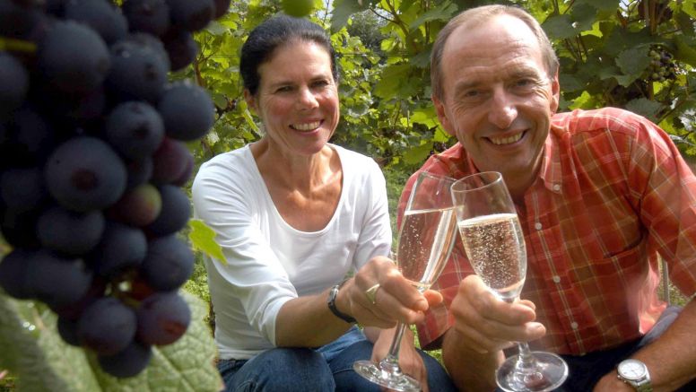 A man and woman pose with glasses of sparkling wine.