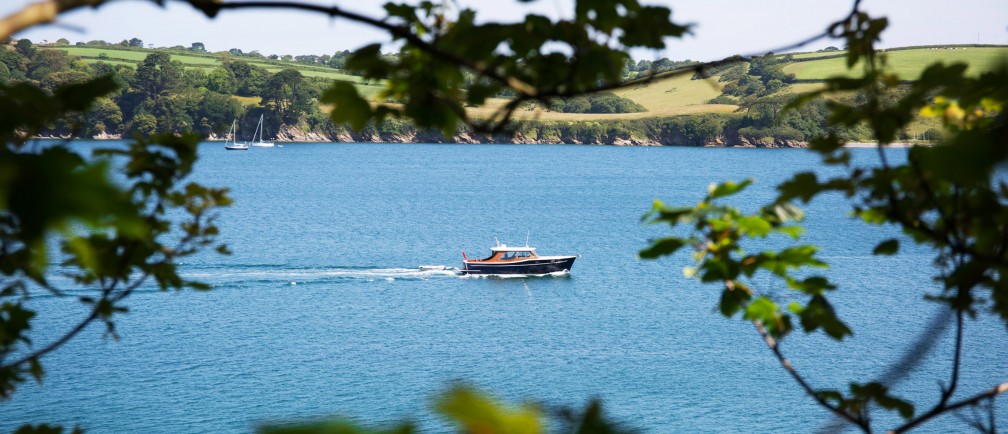 A boat on the River Fal seen through branches.