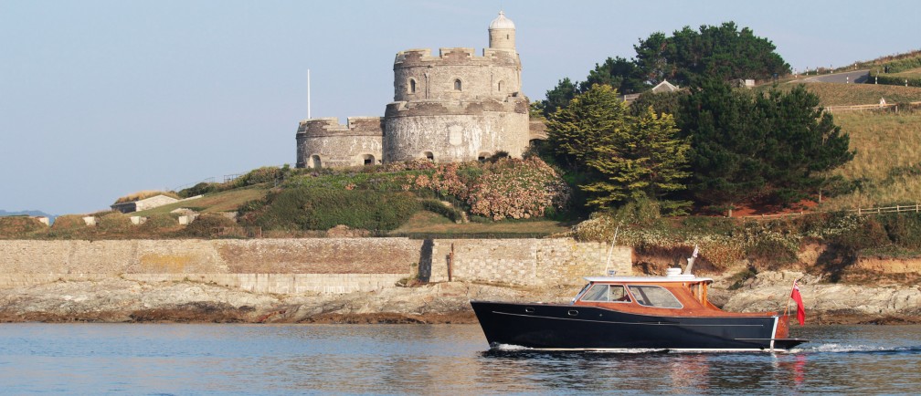 A motor-launch boat sailing slowly past a castle.
