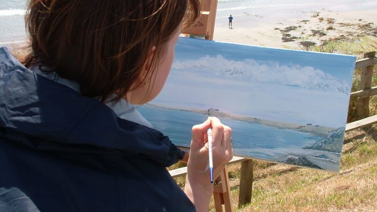 A woman paints the Cornish coast during an art holiday.