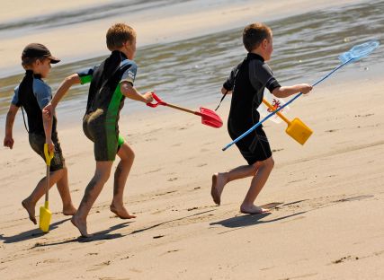 Children run towards the sea at Carne Beach, Cornwall.