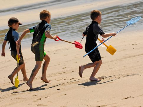 Children run towards the sea at Carne Beach, Cornwall.