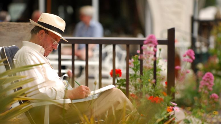 A man writes in a notebook as he sits in The Nare hotel gardens.