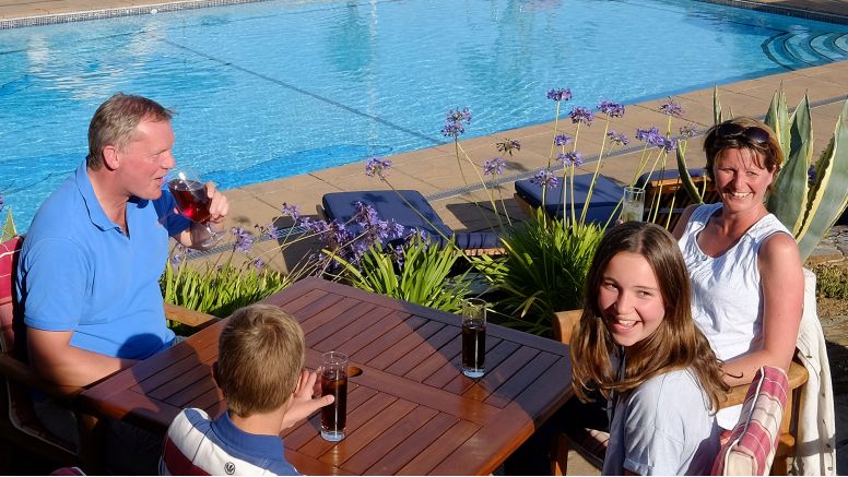 A family enjoys drinks on the terrace by the pool.