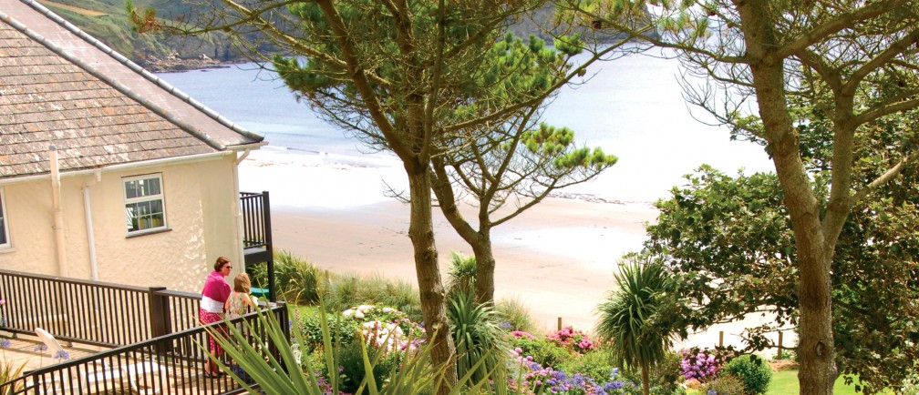 Two guests on the terrace look out at The Nare gardens and Carne Beach.