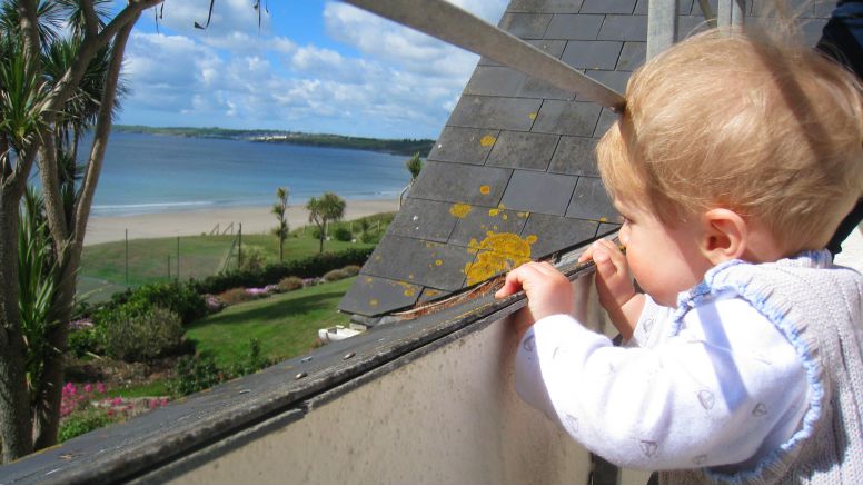 A toddler peering over the edge of a balcony to see the sea views at The Nare Hotel