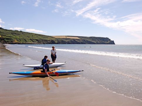 Two holidaymakers sit in kayaks on Carne Beach.