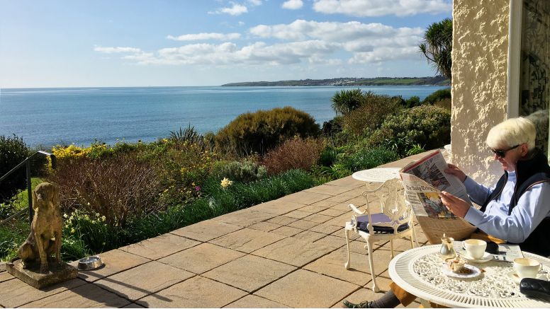 A man relaxing with a newspaper on a sunny terrace at The Nare, Cornwall's five star country house hotel