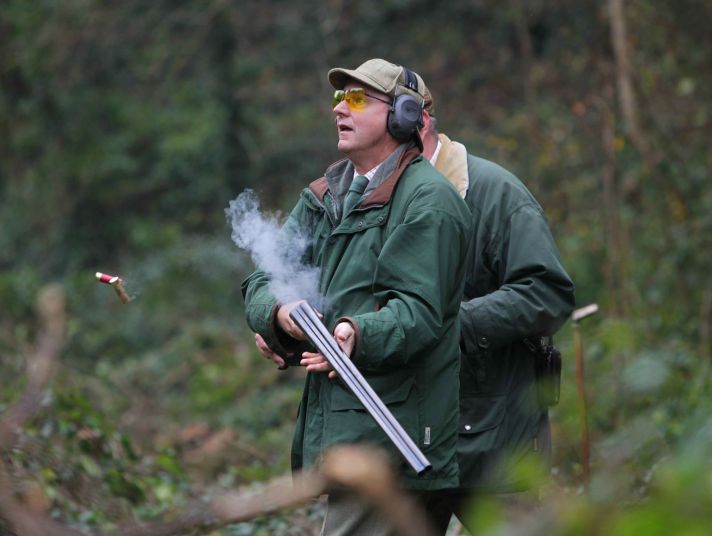 A break-action shotgun sheds shells and puffs smoke in a man's hands.